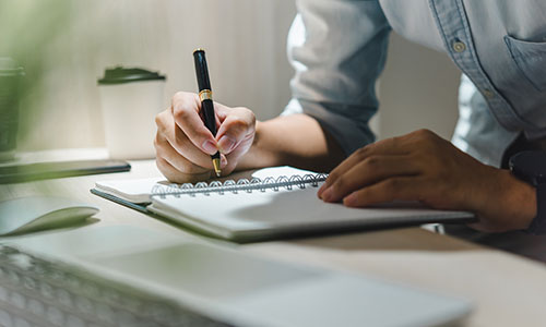 Hand writing notes with a pen in a notebook on a desk, close-up
