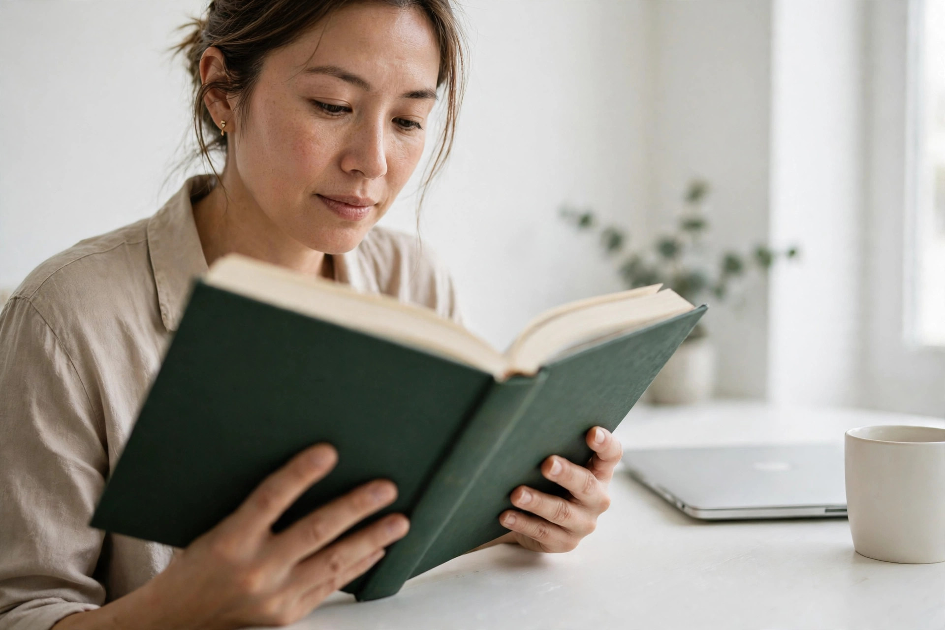 Woman reading a green hardcover book at a white desk in a bright room - The Thinking Machine book review reading scene